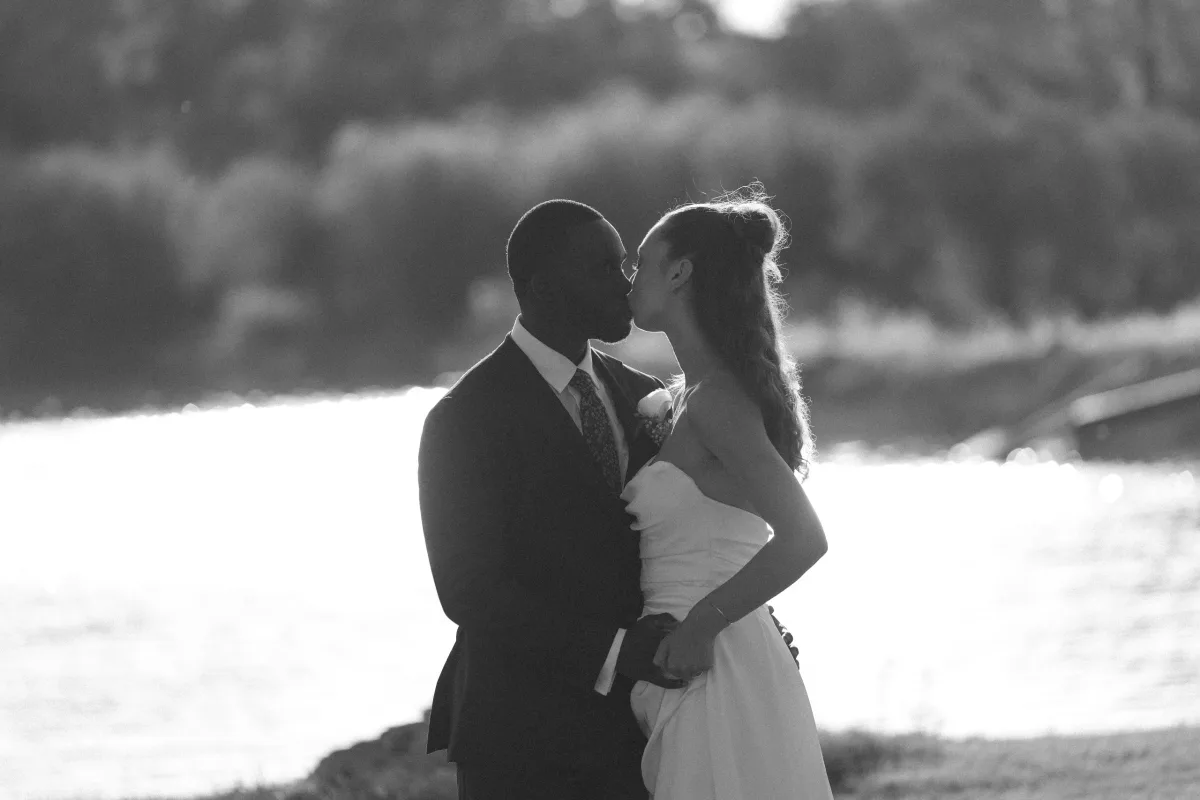 Bride and groom kissing in backlight by the lake at Korineum Golf & Beach Resort, Esentepe · Mert Gardiyanoğlu Photography