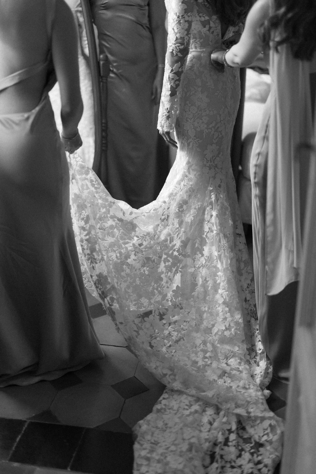 Details — bride being helped into her lace wedding dress by family