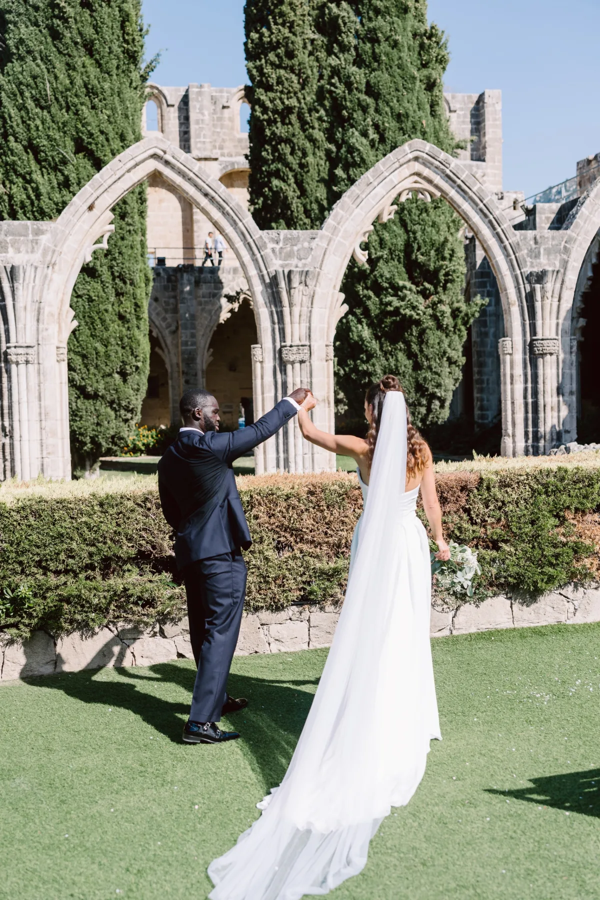 Damat gelinin uzun eteğini savururken, Bellapais Manastırı kemerlerinin önünde — Mert Gardiyanoğlu Photography
